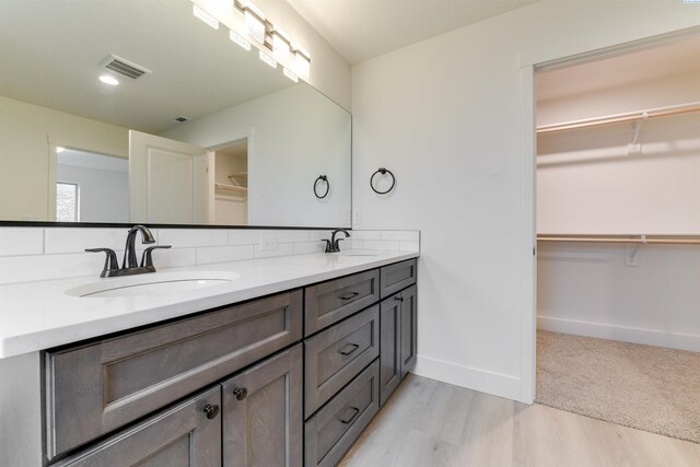 bathroom with wood finished floors, baseboards, double vanity, a spacious closet, and decorative backsplash