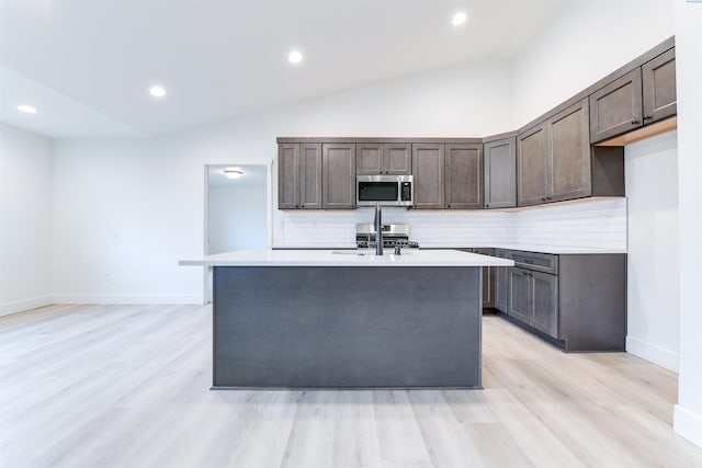 kitchen featuring stainless steel microwave, light countertops, tasteful backsplash, dark brown cabinets, and vaulted ceiling