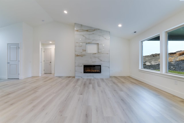 unfurnished living room with lofted ceiling, a premium fireplace, light wood-style flooring, baseboards, and recessed lighting