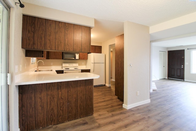 kitchen featuring sink, hardwood / wood-style flooring, white appliances, kitchen peninsula, and a textured ceiling