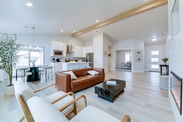 living room with beamed ceiling, plenty of natural light, an inviting chandelier, and light hardwood / wood-style flooring