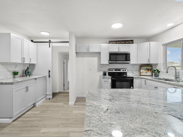 kitchen with sink, light stone counters, black range with electric cooktop, a barn door, and white cabinets