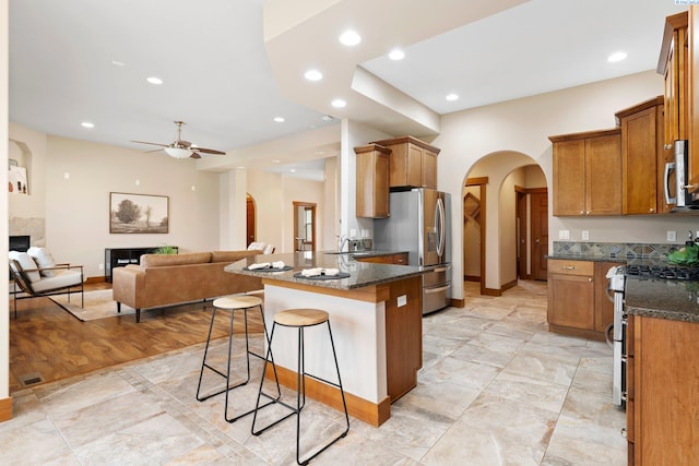 kitchen with appliances with stainless steel finishes, dark stone countertops, a kitchen breakfast bar, ceiling fan, and kitchen peninsula