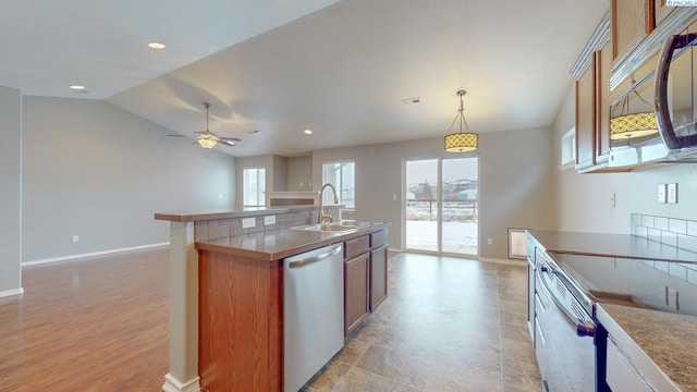 kitchen featuring lofted ceiling, appliances with stainless steel finishes, sink, decorative light fixtures, and an island with sink