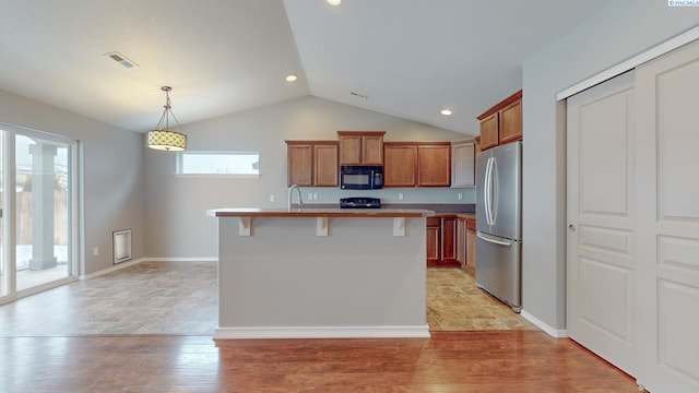 kitchen with a center island with sink, a kitchen bar, vaulted ceiling, stainless steel fridge, and hanging light fixtures