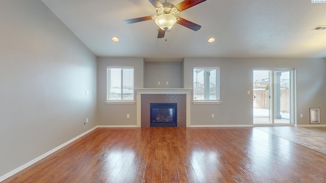 unfurnished living room featuring ceiling fan, hardwood / wood-style flooring, a brick fireplace, and a wealth of natural light