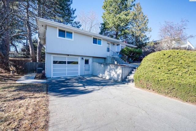 view of front of house with a garage, driveway, fence, and central AC unit