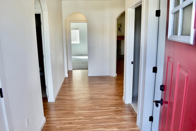 hallway with arched walkways, light wood-style floors, and baseboards