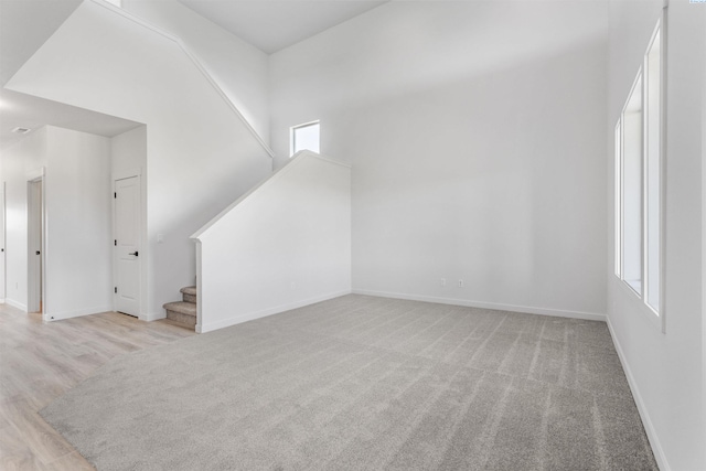 additional living space with baseboards, stairway, plenty of natural light, and light colored carpet