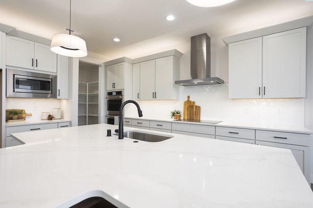 kitchen featuring light stone counters, appliances with stainless steel finishes, sink, and wall chimney range hood