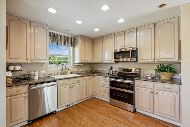 kitchen with stainless steel appliances, a sink, light wood finished floors, dark stone countertops, and recessed lighting