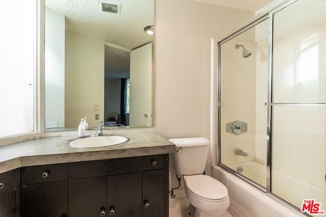 full bathroom featuring vanity, bath / shower combo with glass door, and toilet