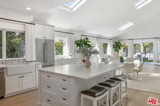 kitchen featuring white cabinetry, light hardwood / wood-style floors, sink, stainless steel appliances, and lofted ceiling with skylight