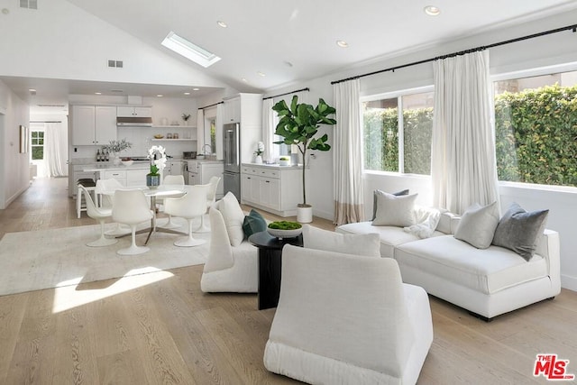 living room with high vaulted ceiling, light wood-type flooring, and a skylight