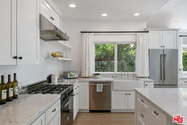 kitchen featuring light stone countertops, high end appliances, tasteful backsplash, white cabinets, and light wood-type flooring