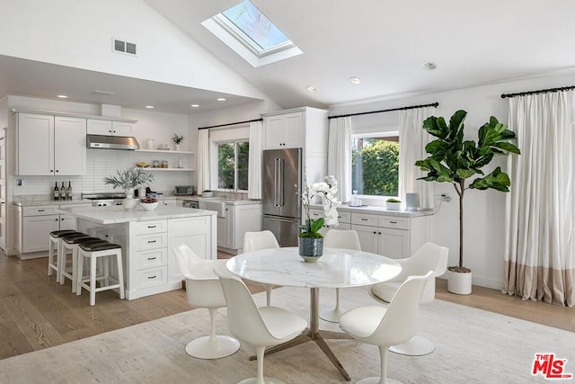 dining area with light hardwood / wood-style flooring, a wealth of natural light, and a skylight