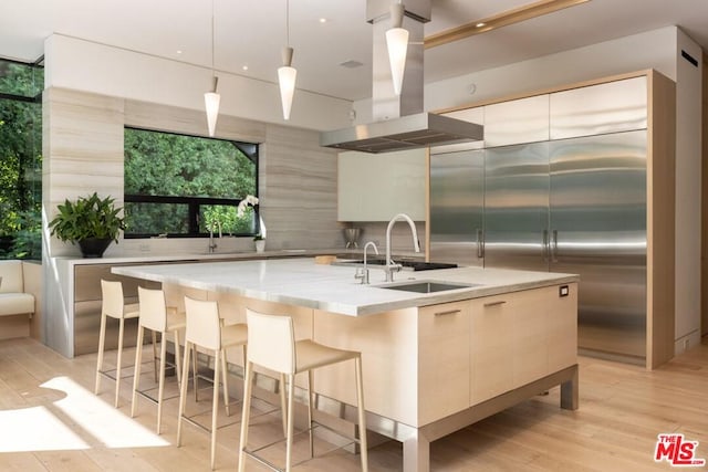 kitchen with a center island with sink, decorative light fixtures, light wood-type flooring, and island range hood