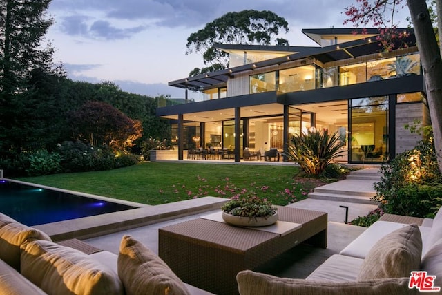 back house at dusk with an outdoor hangout area, a lawn, and a patio