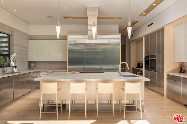 kitchen with stainless steel appliances, decorative light fixtures, a breakfast bar area, a kitchen island with sink, and sink