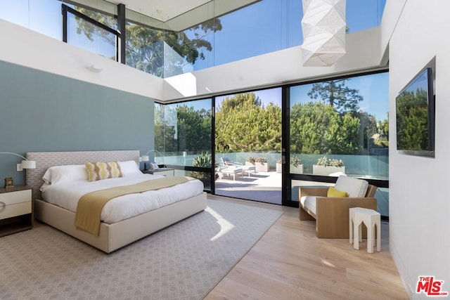 bedroom featuring a high ceiling, access to exterior, and light hardwood / wood-style floors