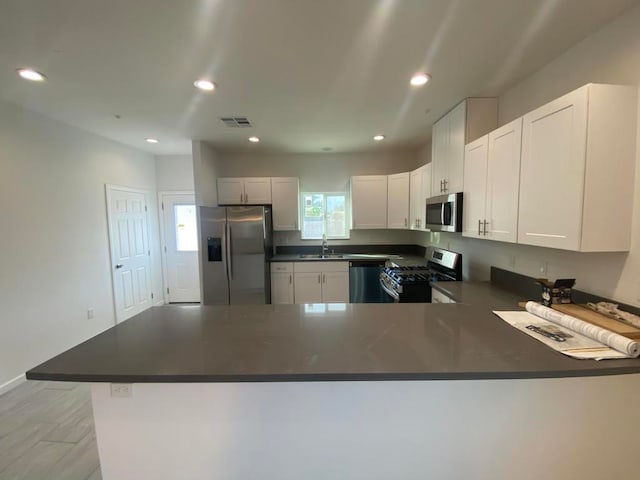 kitchen with appliances with stainless steel finishes, sink, kitchen peninsula, and white cabinets