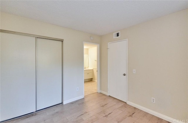 unfurnished bedroom featuring a textured ceiling, light hardwood / wood-style floors, and a closet