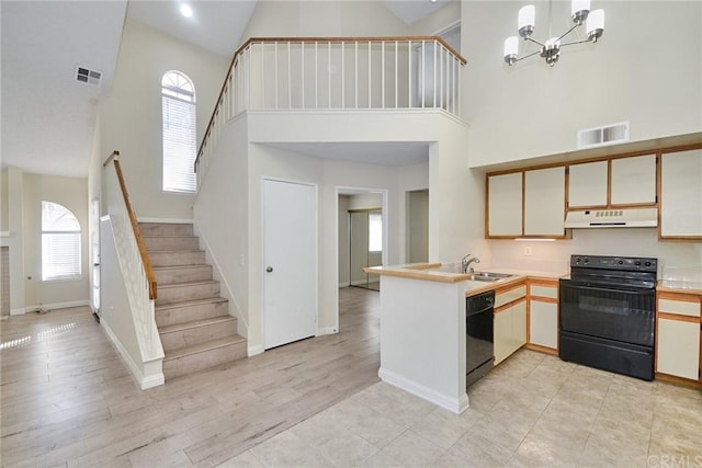 kitchen with light hardwood / wood-style flooring, a notable chandelier, a high ceiling, and black appliances