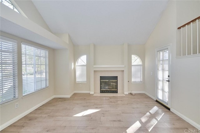 unfurnished living room featuring high vaulted ceiling, a tiled fireplace, and light wood-type flooring