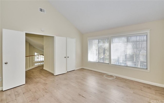 empty room with high vaulted ceiling and light hardwood / wood-style floors