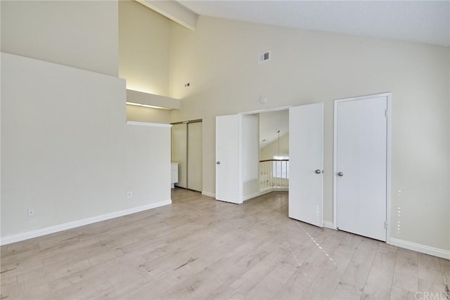 unfurnished bedroom with high vaulted ceiling, light hardwood / wood-style floors, and two closets