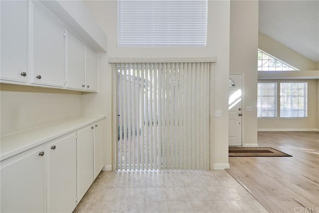 interior space with light wood-type flooring, high vaulted ceiling, and white cabinets