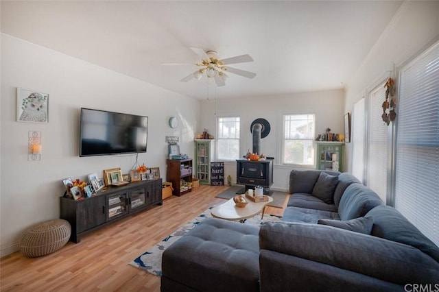 living room with light hardwood / wood-style flooring, ceiling fan, and a wood stove