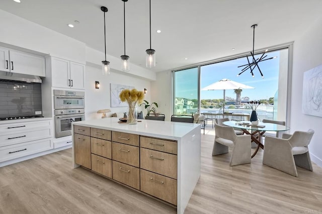 kitchen featuring hanging light fixtures, tasteful backsplash, light hardwood / wood-style floors, stainless steel double oven, and white cabinetry