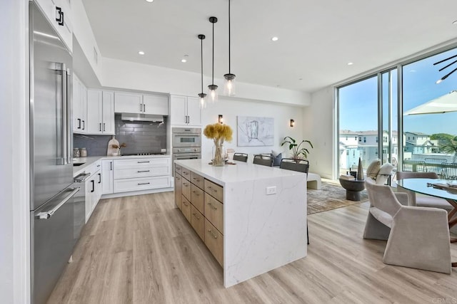 kitchen with stainless steel appliances, light wood-type flooring, a kitchen island, and white cabinets