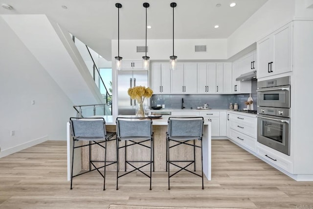 kitchen with hanging light fixtures, backsplash, light hardwood / wood-style flooring, a kitchen island, and a breakfast bar area