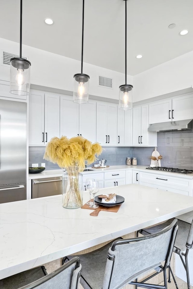 kitchen with decorative light fixtures, backsplash, a kitchen bar, and white cabinets