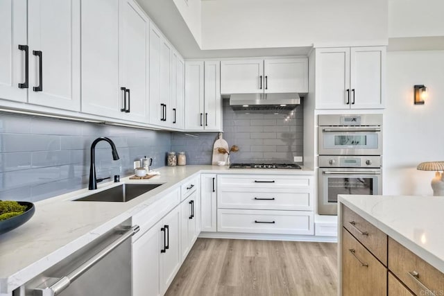 kitchen featuring white cabinets, backsplash, light hardwood / wood-style floors, and light stone countertops