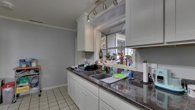 kitchen featuring sink, light tile floors, white cabinets, dark stone countertops, and crown molding