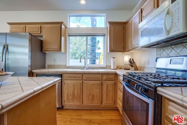 kitchen with tile countertops, stainless steel appliances, light wood-type flooring, and sink