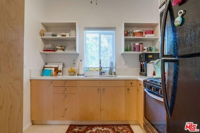 kitchen with light tile flooring, stainless steel gas range, sink, and black fridge