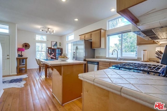 kitchen featuring tile counters, a kitchen island, a kitchen breakfast bar, appliances with stainless steel finishes, and light hardwood / wood-style floors