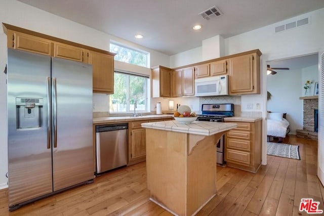 kitchen featuring ceiling fan, a fireplace, appliances with stainless steel finishes, tile countertops, and a kitchen island