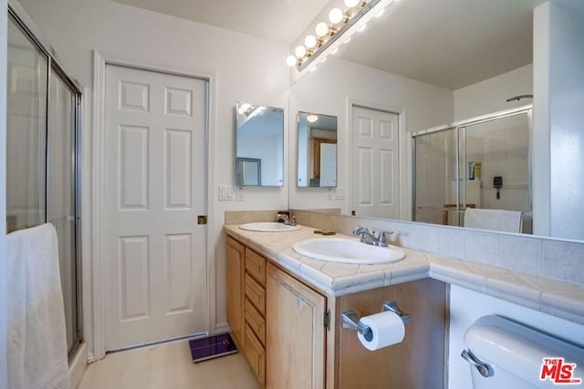 bathroom featuring tile floors, double sink vanity, toilet, and an enclosed shower