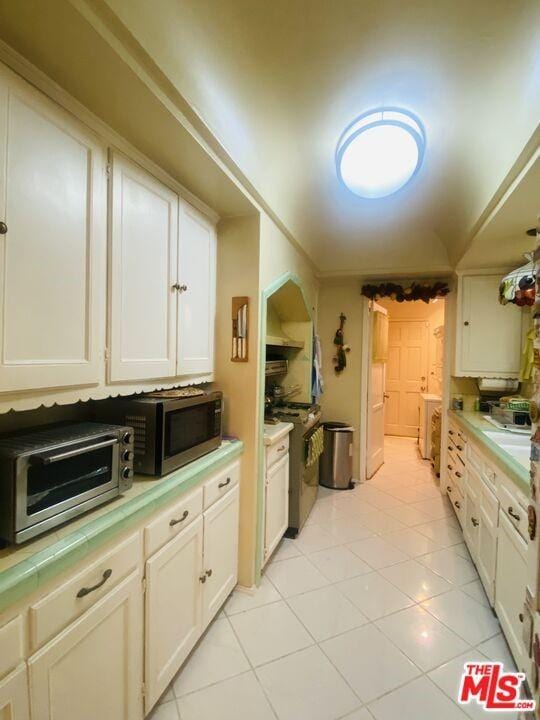 kitchen featuring stove, white cabinetry, and light tile flooring