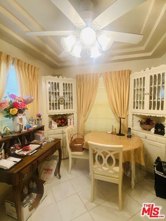 sitting room featuring ceiling fan, a raised ceiling, and light tile floors