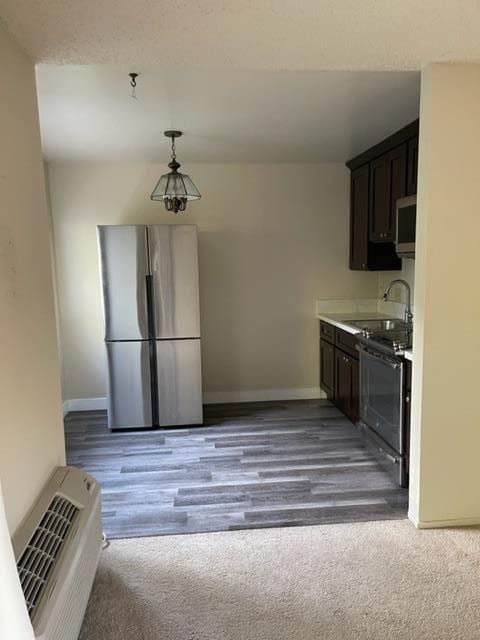 kitchen featuring light carpet, hanging light fixtures, dark brown cabinetry, and stainless steel appliances