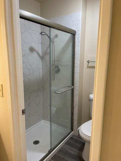 bathroom with toilet, an enclosed shower, and wood-type flooring