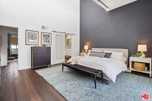 bedroom with dark hardwood / wood-style flooring, a towering ceiling, rail lighting, and a barn door