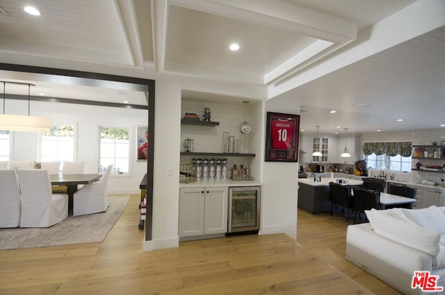 bar featuring hanging light fixtures, sink, beverage cooler, light hardwood / wood-style flooring, and white cabinetry