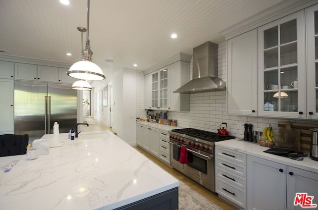 kitchen featuring tasteful backsplash, high end appliances, decorative light fixtures, sink, and wall chimney range hood